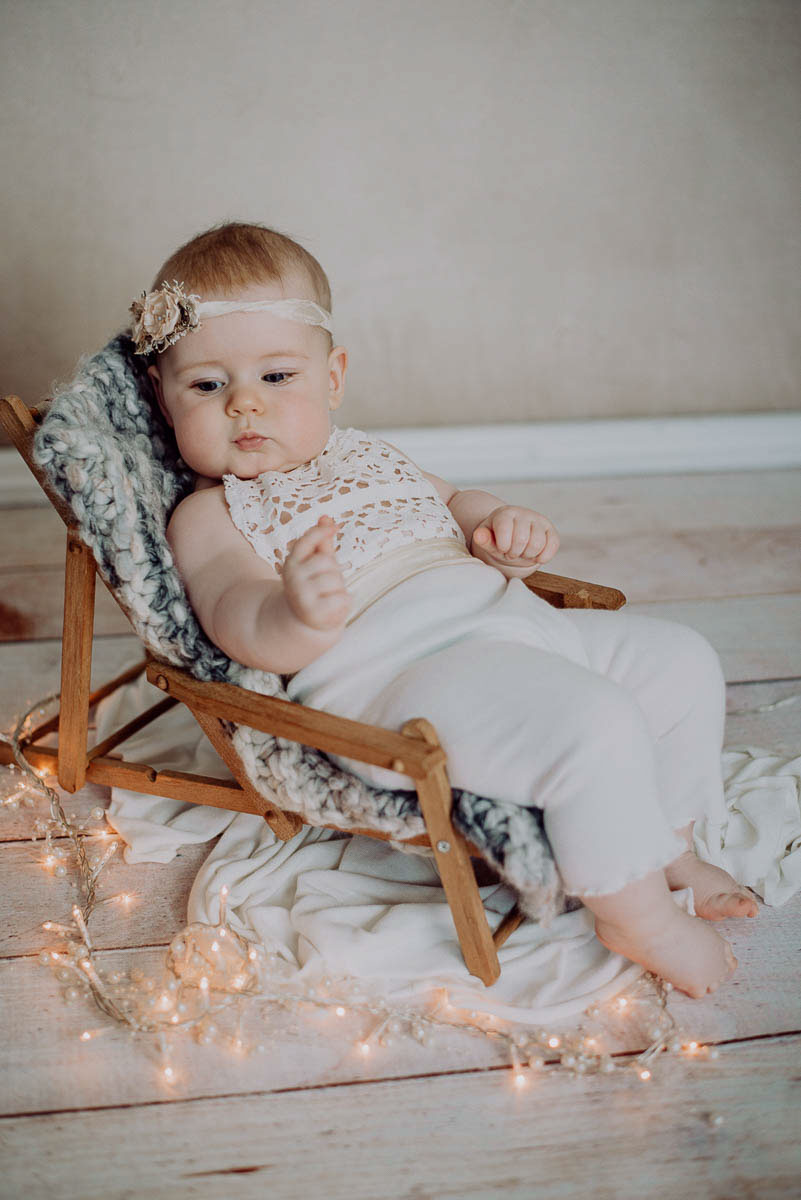 Familien Fotoshooting Mädchen auf Babyliegestuhl in weißem Strampler mit weihnachtlicher Lichterkette Weihnachtsfotoshooting