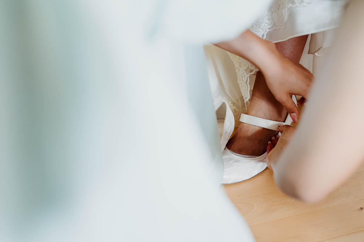 Trauzeugin zieht während des Getting Ready der Braut die Brautschuhe an.