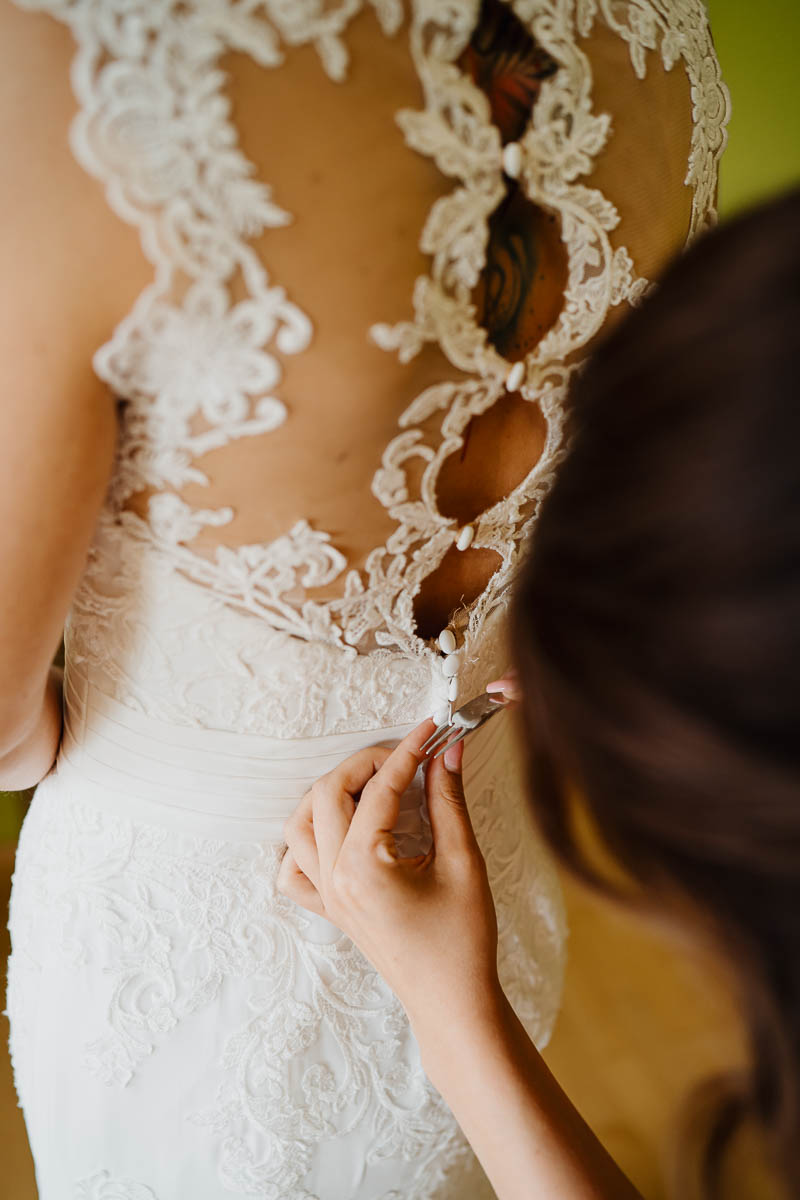 Nahaufnahme von aufgeregten Händen beim Schließen der Knöpfe am Brautkleid.